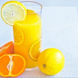 Vibrant citrus juice in a glass with fresh orange and lemon slices, offering a refreshing taste of summer.